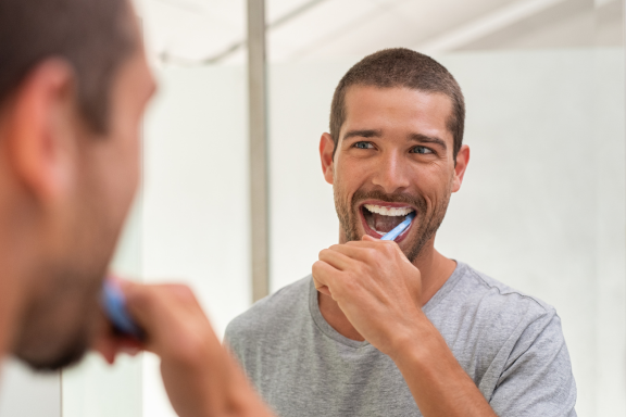 man brushing his teeth after wisdom teeth removal services following post operative instructions