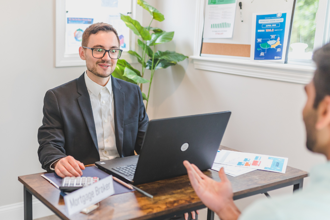 Business broker meeting with client across desk in modern office with charts and laptop