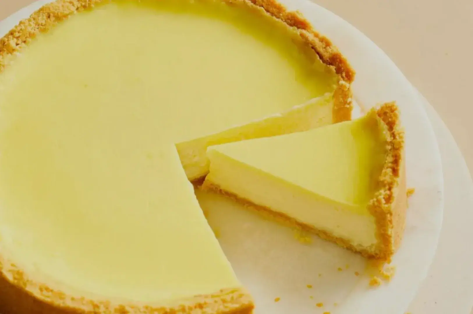 A round new york cheesecake with a slice cut out, sitting on a white plate.