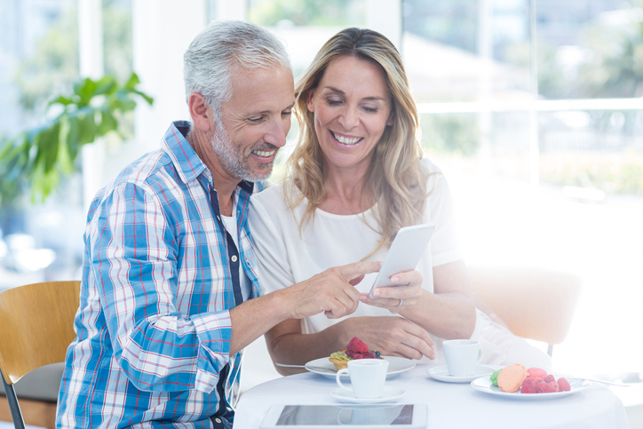 Mature couple having breakfast and smiling at a cell phone. 