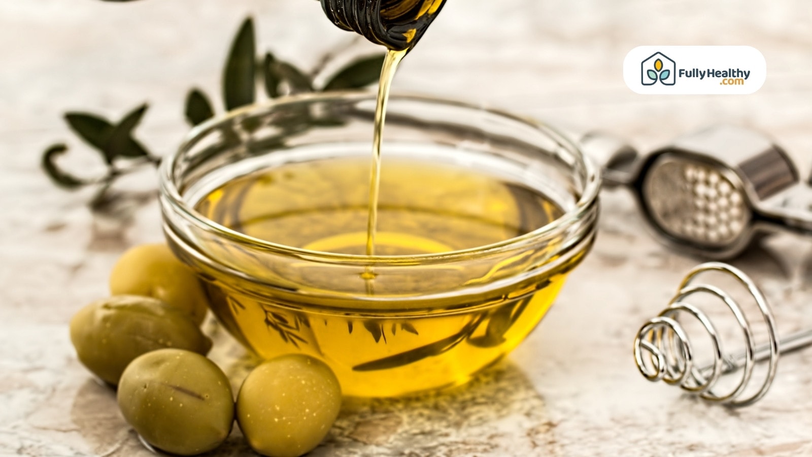 Olive oil being poured into glass bowl with green olives beside