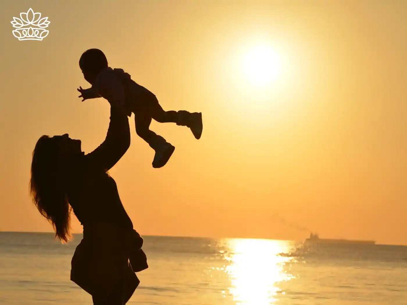 A silhouette of a mother lifting her child up against a golden sunset backdrop. Fabulous Flowers and Gifts. Mother's Day Flowers.