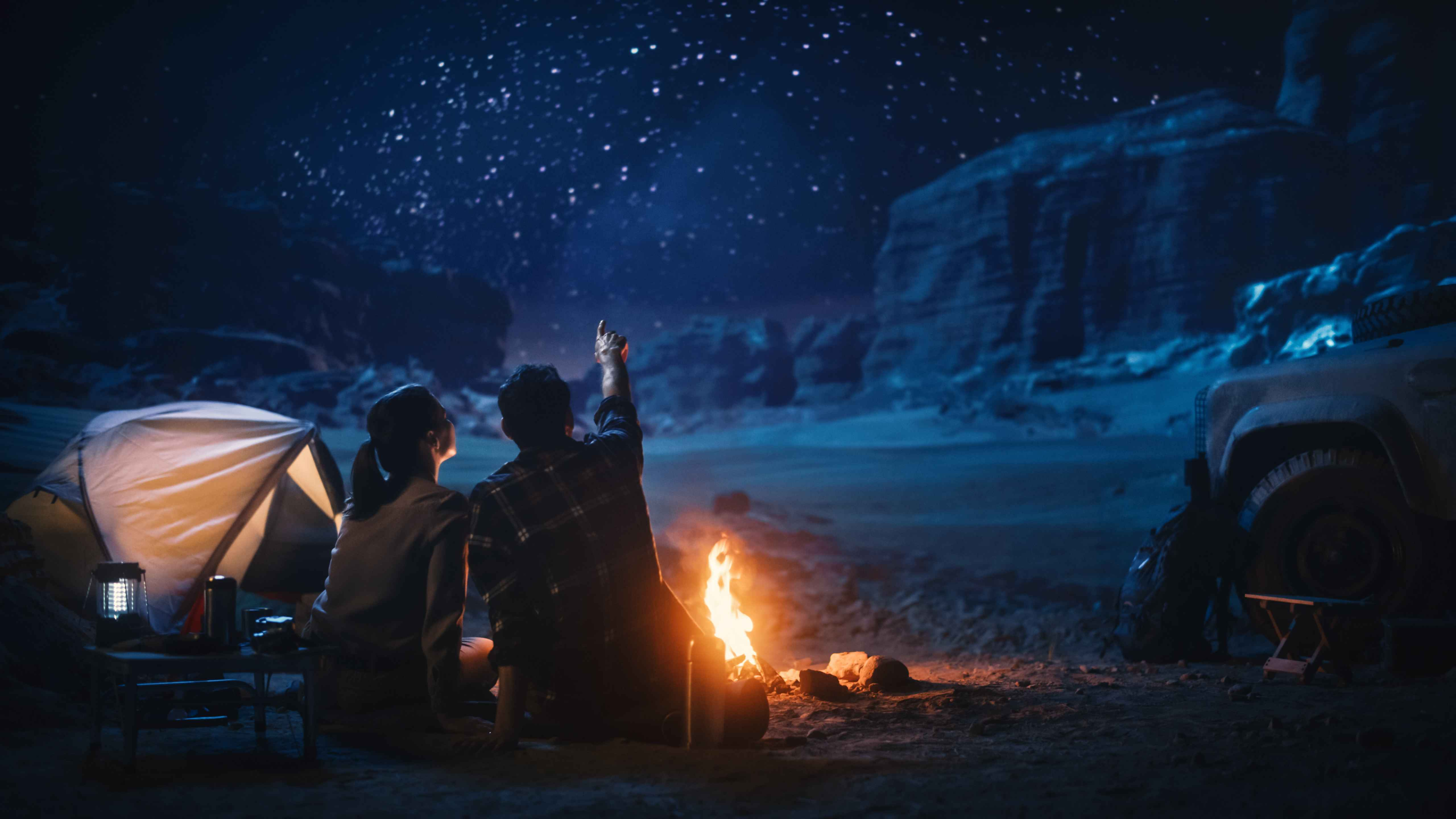 Acampamento feliz: Casal sentado junto à fogueira e a olhar para as estrelas