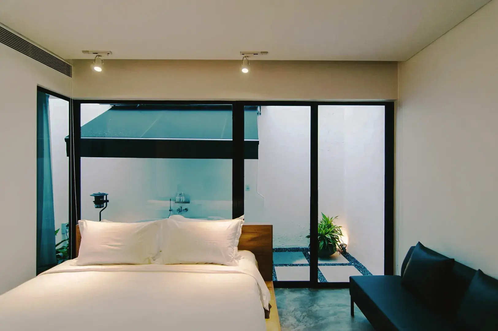Modern minimalist bedroom in Singapore with white bedding, glass doors, and private courtyard view.