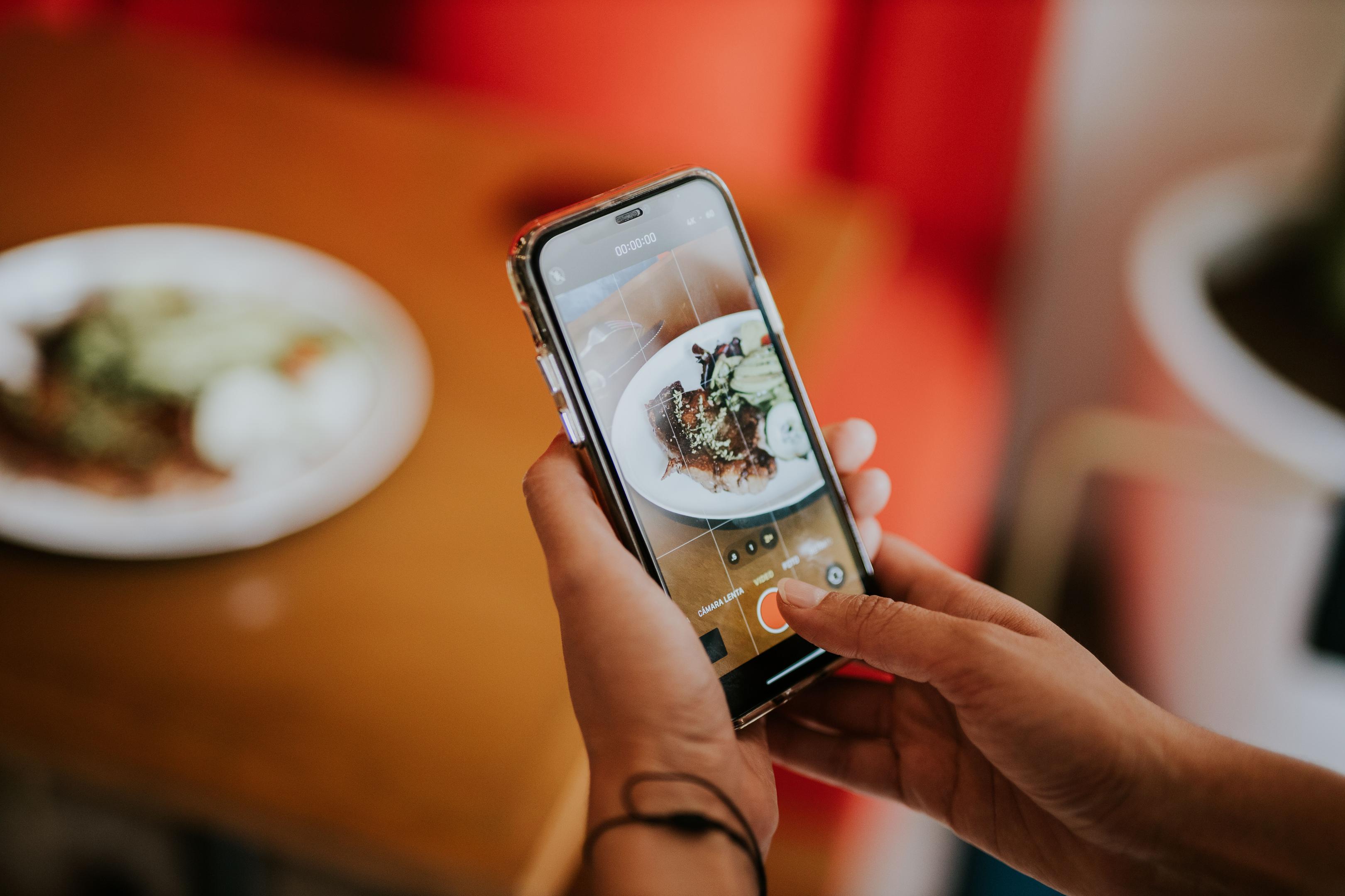 A person is seated at a cafe table, intently holding a smartphone that displays a food ordering screen, showcasing an online ordering system. This scene reflects the modern dining experience where customers can conveniently explore a restaurant's menu and place orders directly from their mobile devices.