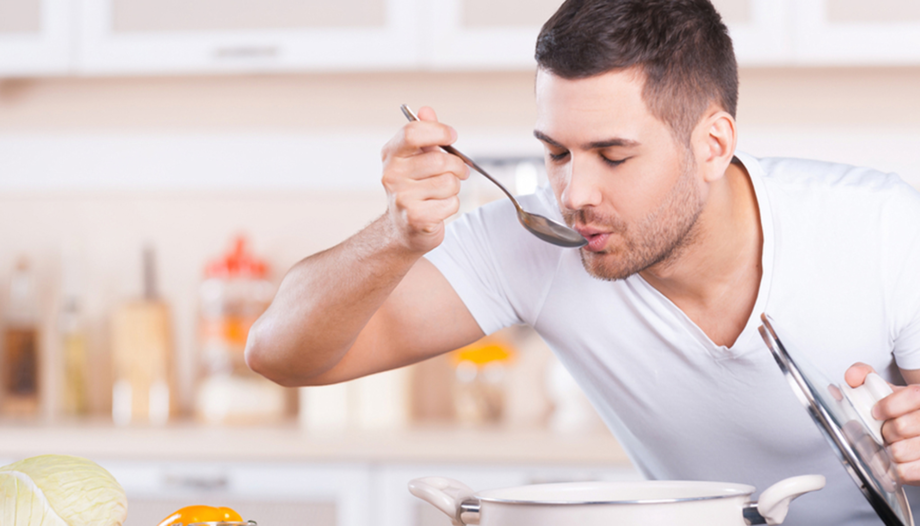Mistet Smak og Luktesans: Hvordan Det Påvirker Munnhelsen 14 Mann smaker på suppe med skje på kjøkken mens han holder lokk over gryte.