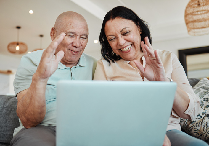 Happy older couple sitting on the sofa Facetiming with their daughter. 