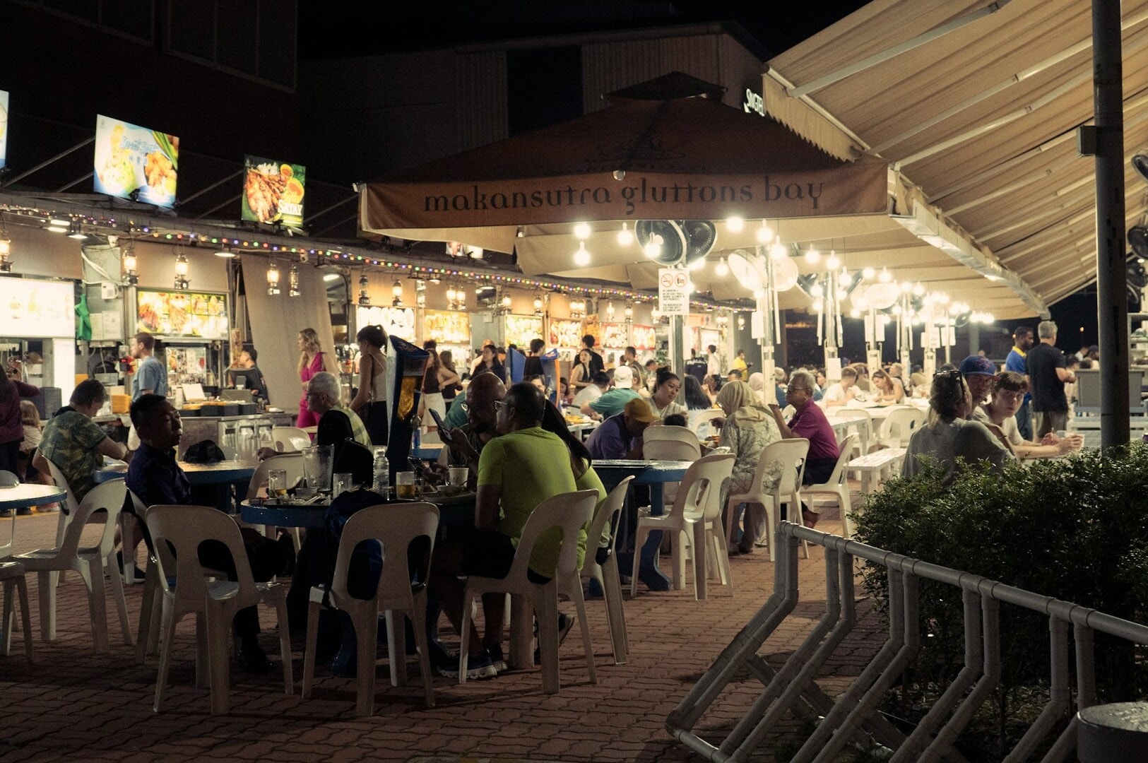 People dining at tables in a bustling Singapore Hawker Centre, enjoying a variety of local street food.