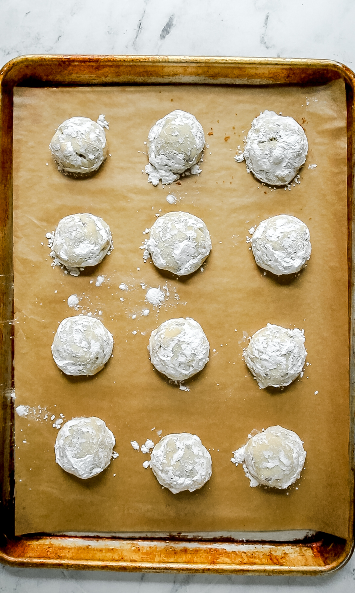 12 baked chocolate chip snowball cookies on a baking sheet with parchment paper