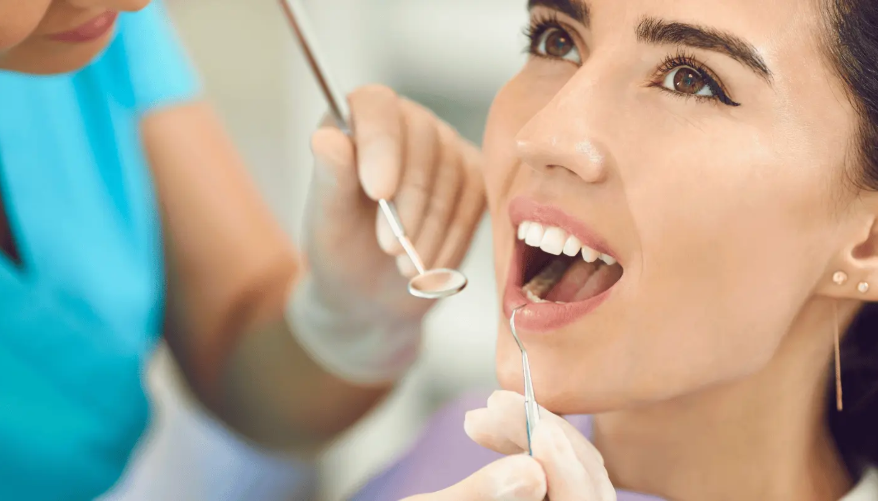 Kvinne som undersøkes hos tannlege, åpen munn med tannlegeinstrumenter i bruk under tannbehandling.