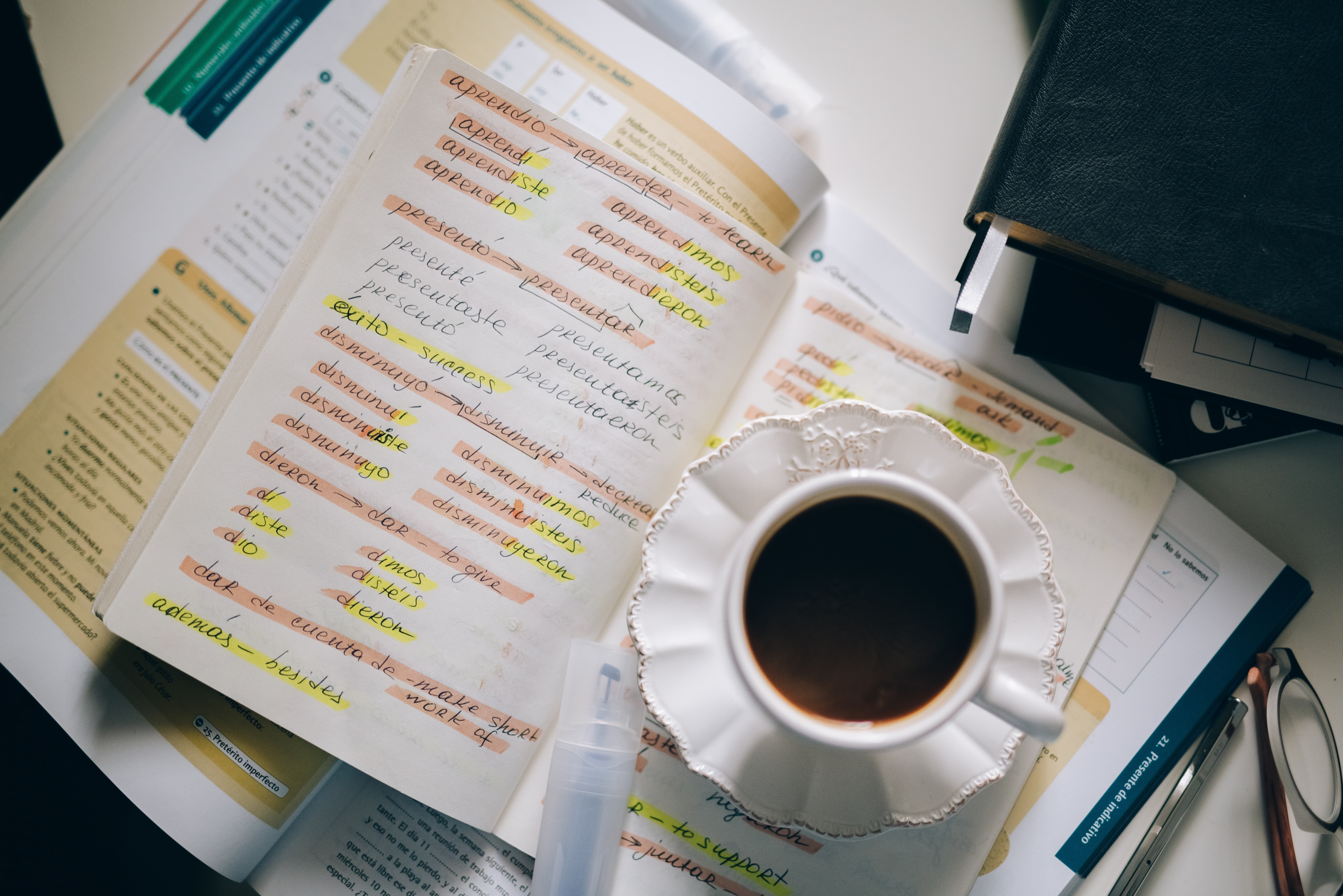 A cup of coffee on a notebook and language learning textbook.