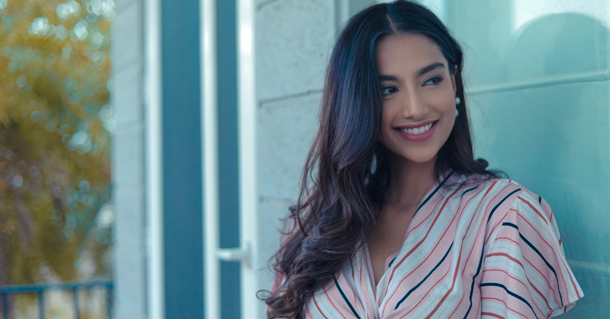 Smiling woman with long, dark hair and a striped shirt standing outdoors next to a window, discussing tax solutions.