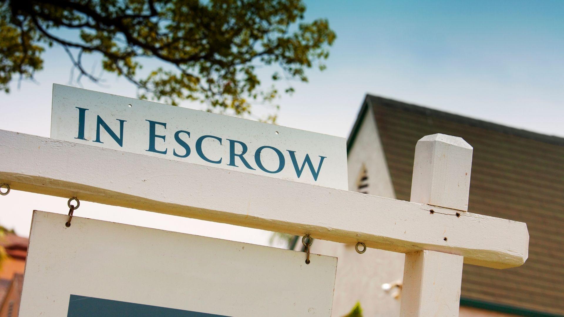Real estate sign displaying “In Escrow” outside a residential property, indicating a home sale is in progress.
