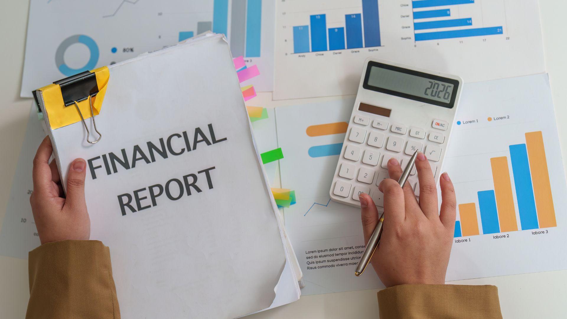 Hands reviewing financial report charts and calculator while analyzing investment property metrics like debt service coverage ratio and gross rent multiplier.