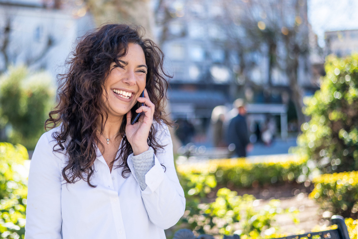 Woman with long dark hair smiling and talking on a cell phone. 