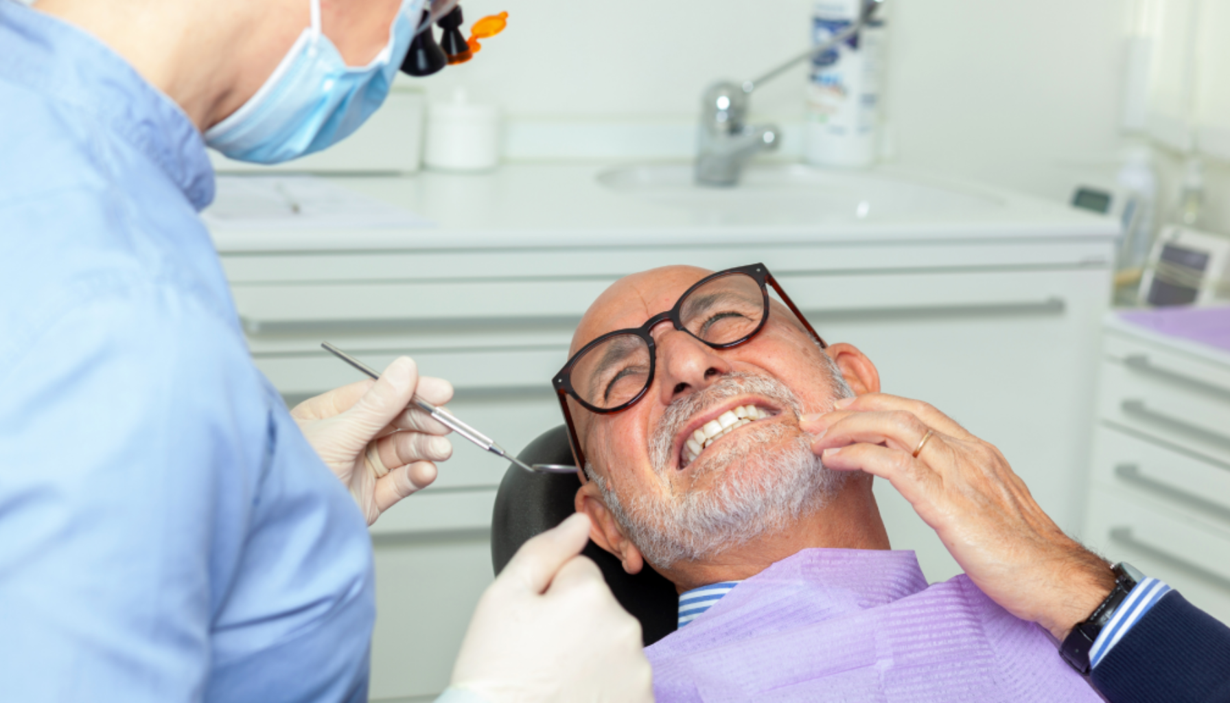 Eldre mann hos tannlegen viser smerte mens tannlegen undersøker munnen med instrumenter i en klinisk setting.