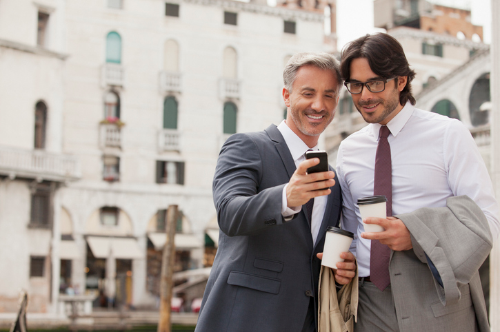 Two businessmen chatting on a city street and having coffee. 