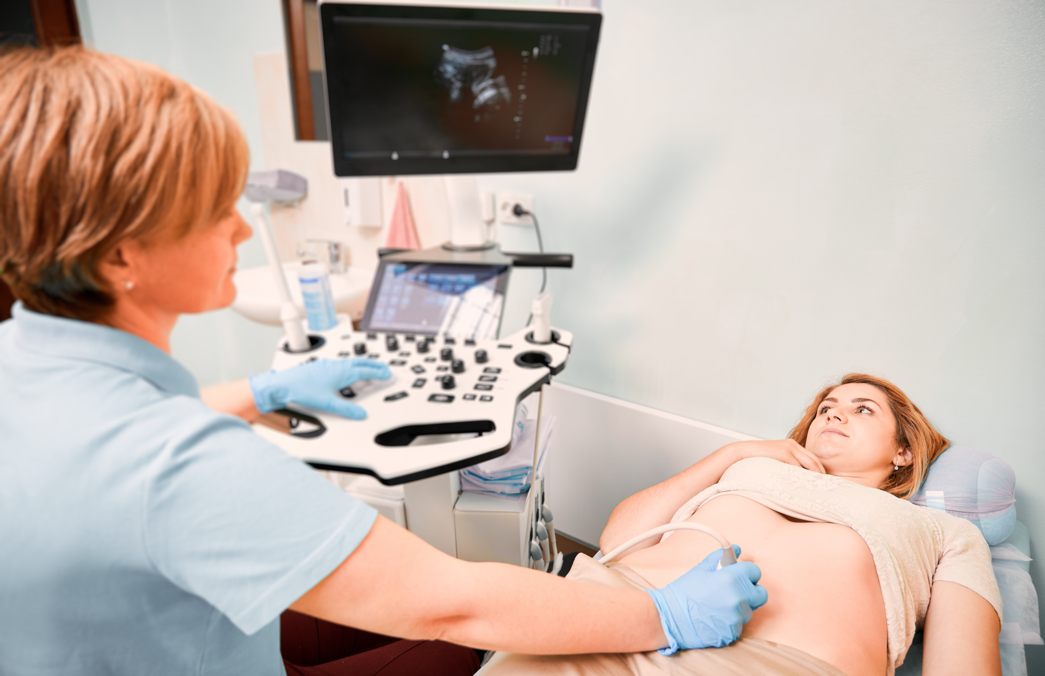 A female doctor performing an abdominal examination of a female patient.