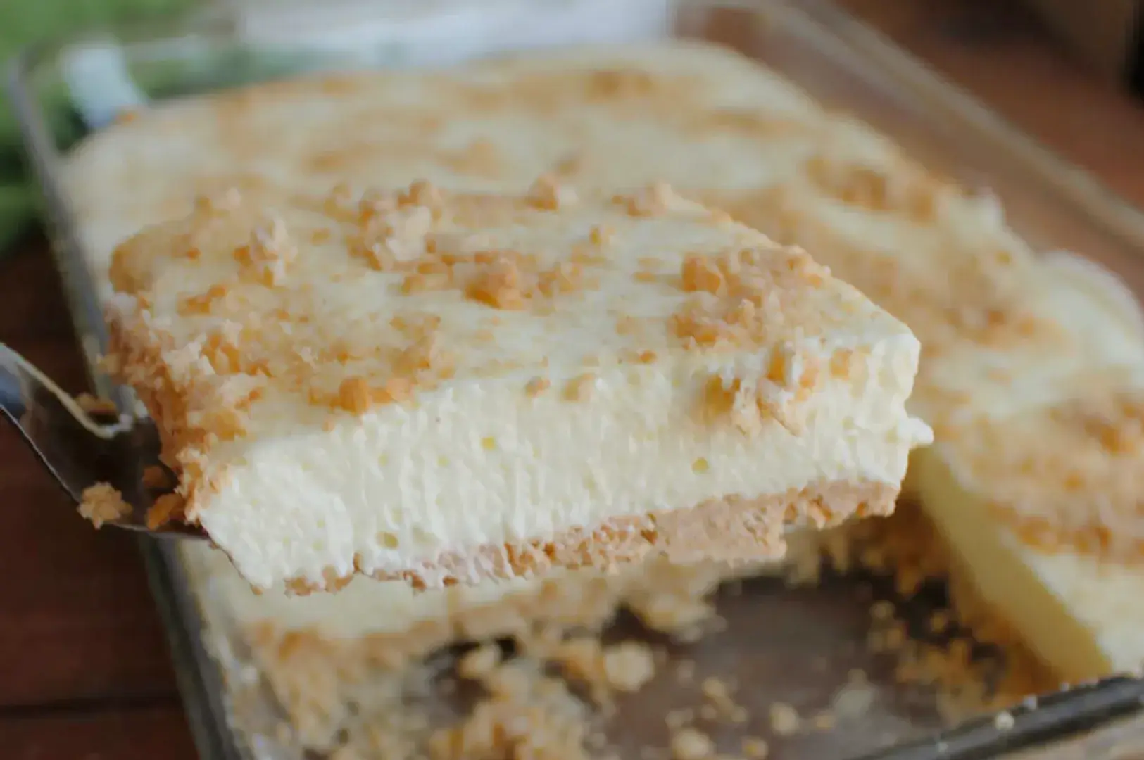 A slice of layered dessert with a creamy filling and a crumbly topping being served from a dish.
