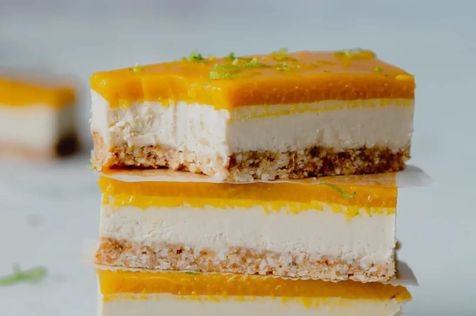 A stack of two layers of cheesecake with a mango topping, sitting on a white surface.