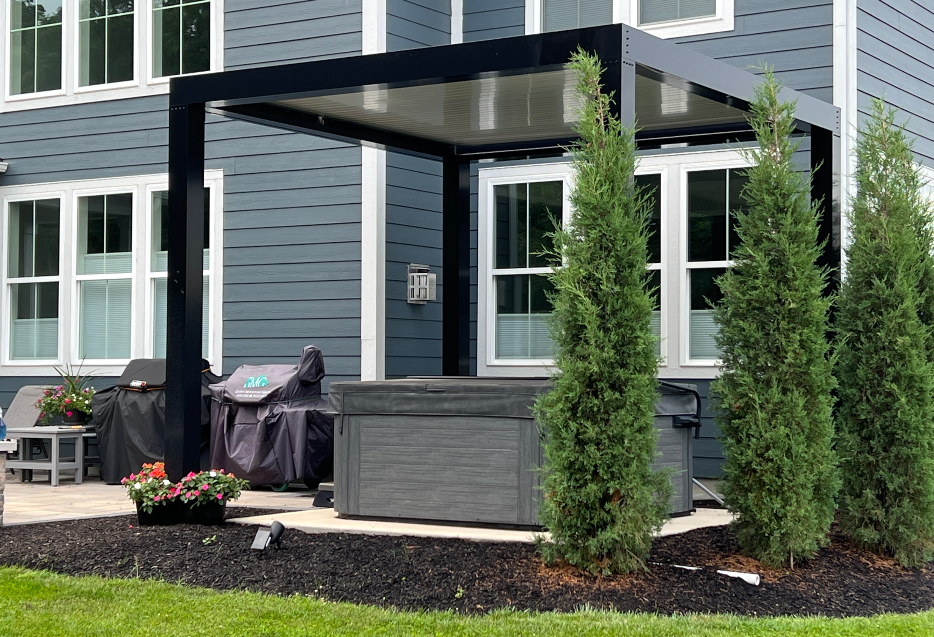 Black hot tub pergola with landscaping for privacy.