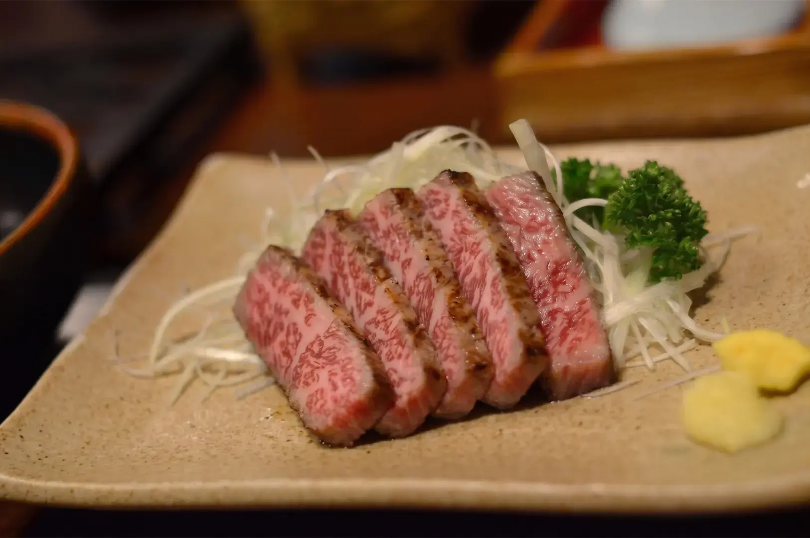 Slices of A4 Miyazaki Wagyu striploin, seared and served with shredded scallions and mustard on a rustic plate.