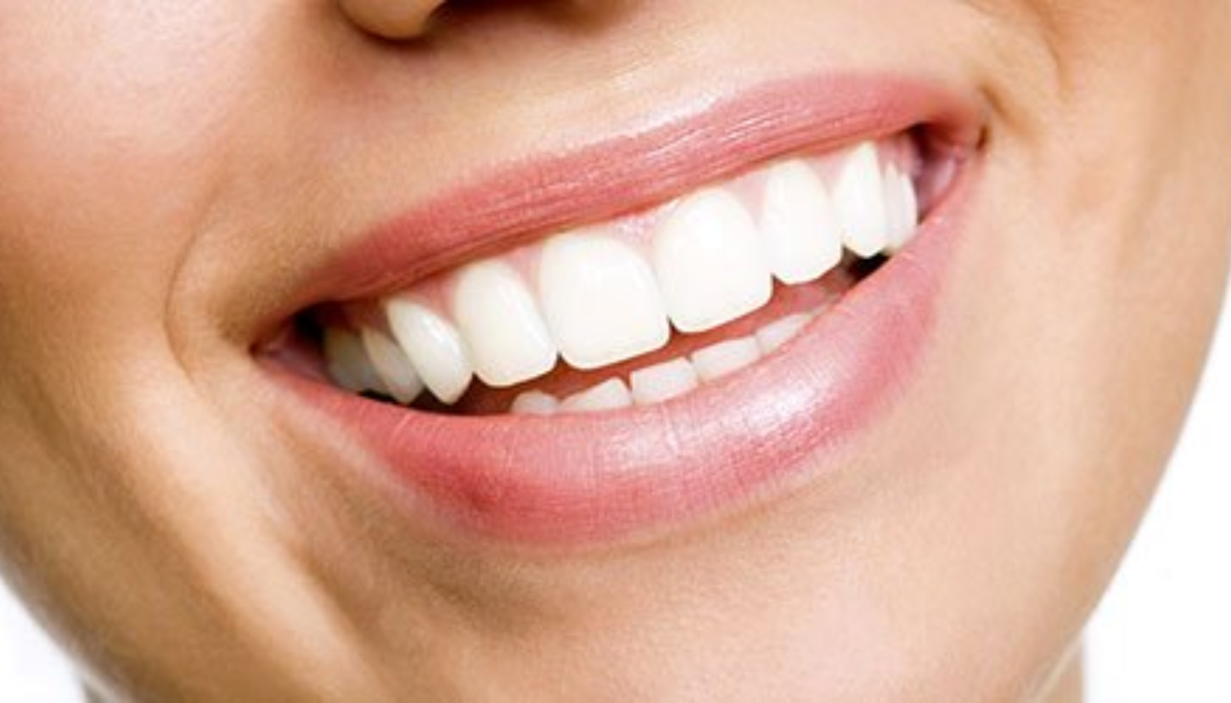 Erosjon på Tennene: Den Usynlige Skaden Du Ikke Merker Før Det Er For Sent 4 Nærbilde av smilende munn med hvite, rette tenner og sunne lepper.