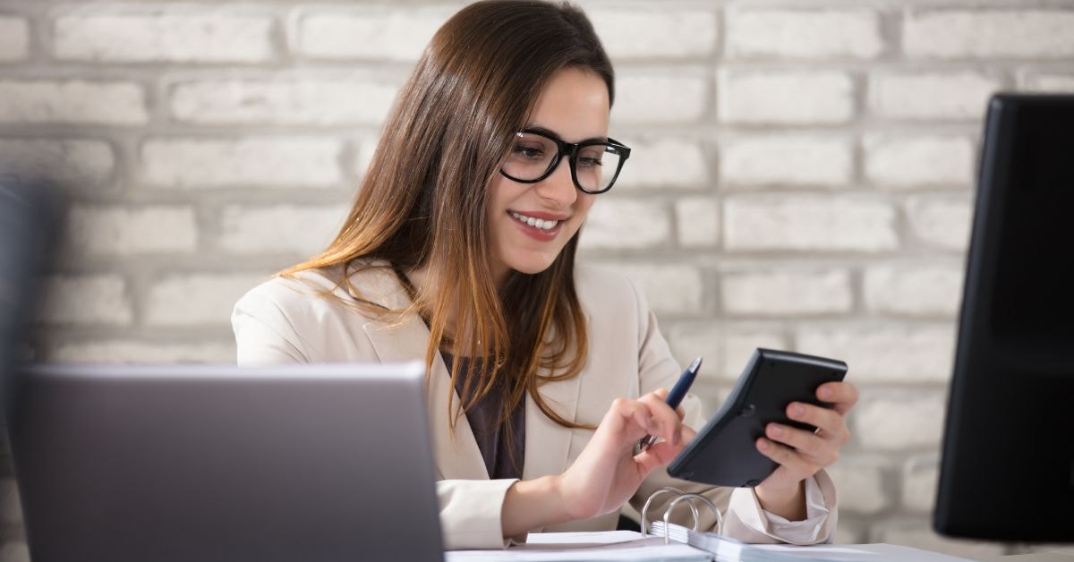 A smiling accountant using a calculator while managing tax basis accounting tasks at her desk.