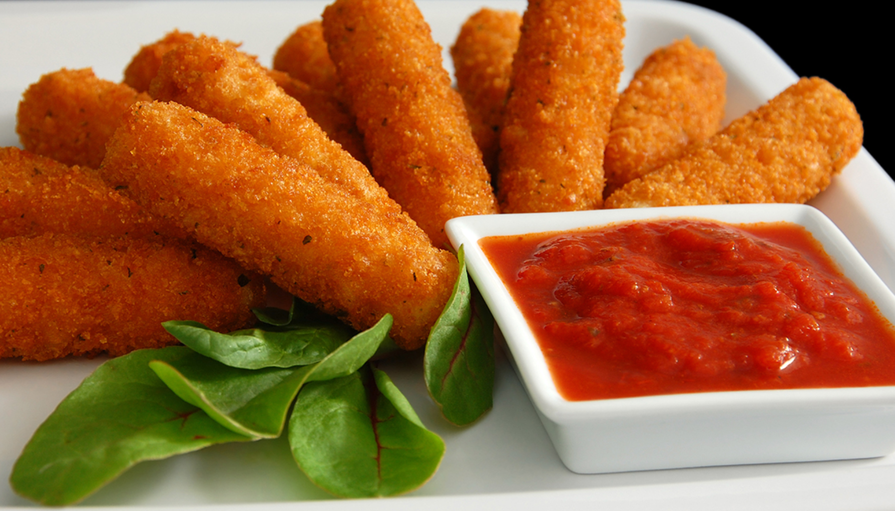 Sprøstekte mozzarella-sticks servert på tallerken med tomatsaus og grønne blader.