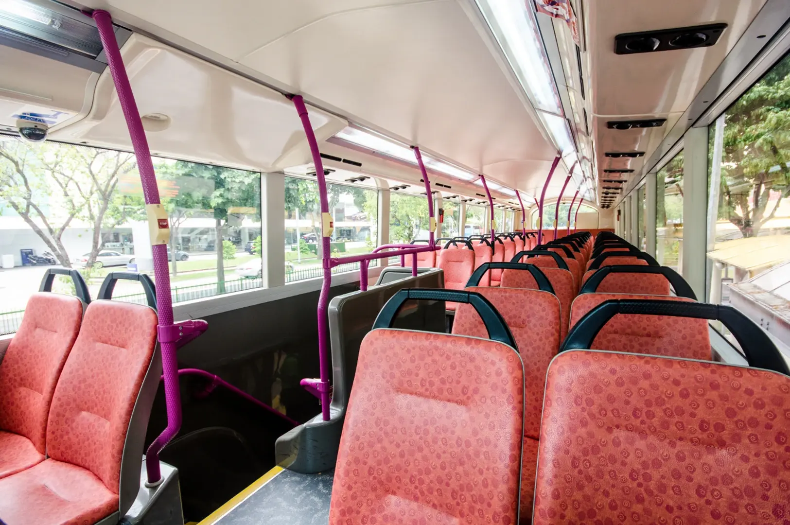 The interior of a bus showing rows of empty red seats with purple support poles and large windows.
