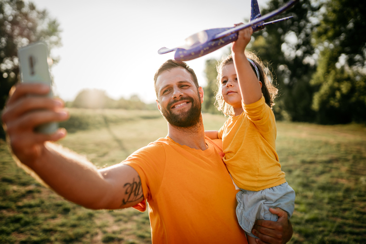 Cheerful young dad and little daughter, both in orange tee shirts, smiling for a selfie in the backyard.   