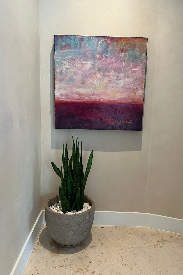 a bold landscape with purple foreground hangs above a plant in a niche