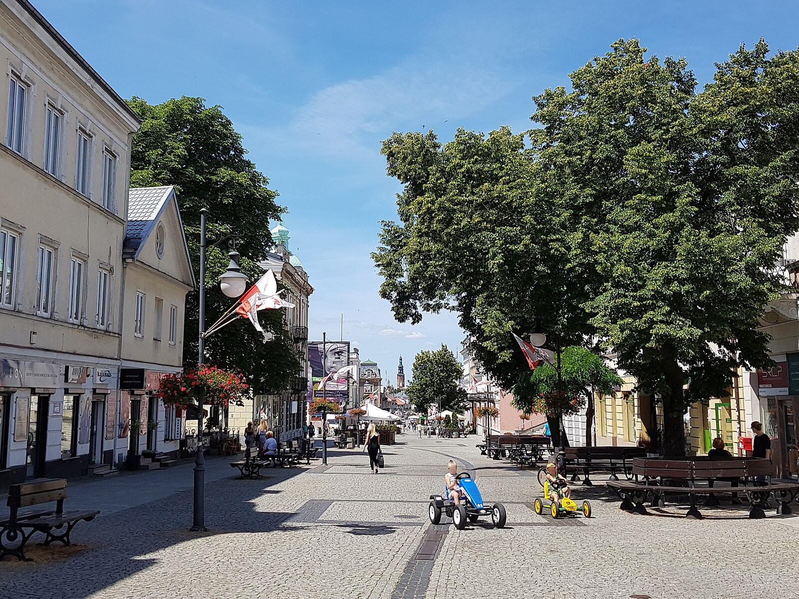 Zdjęcie ulicy Żeromskiego, tętniącej życiem części miasta. Ulicą Żeromskiego przechadzają się dorośli i dzieci. Źródło: https://commons.wikimedia.org/wiki/File:%C5%BBeromski_St_Radom_Poland.jpg