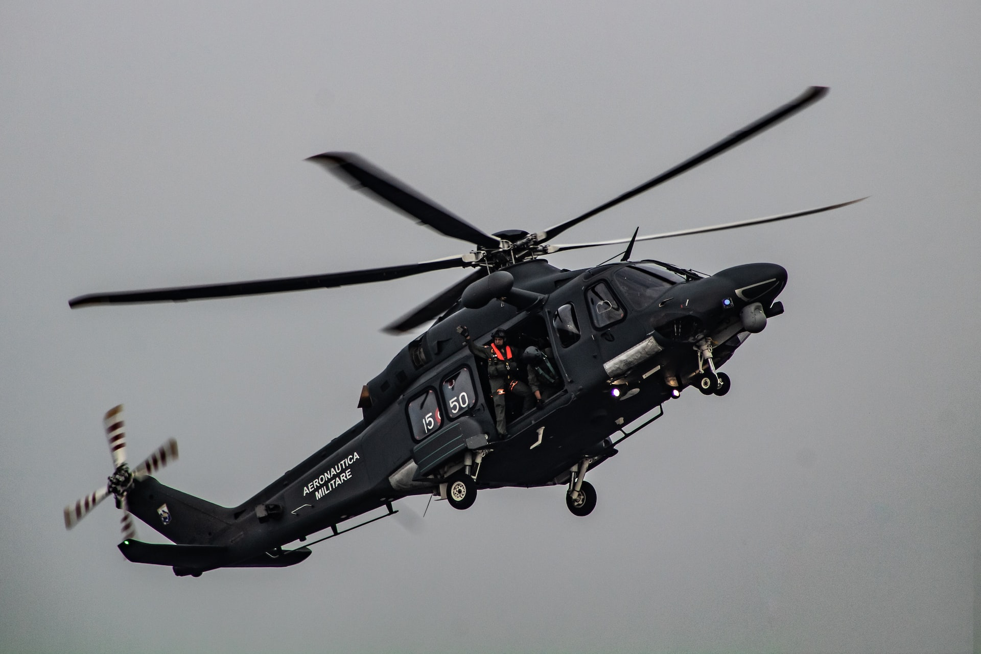 A black military helicopter with crew in flight.