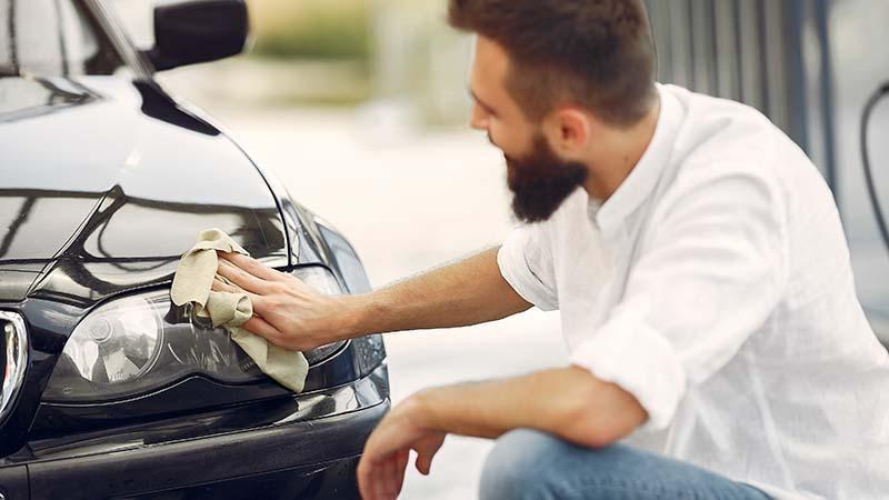 A man cleaning his car's headlights with a microfiber cloth