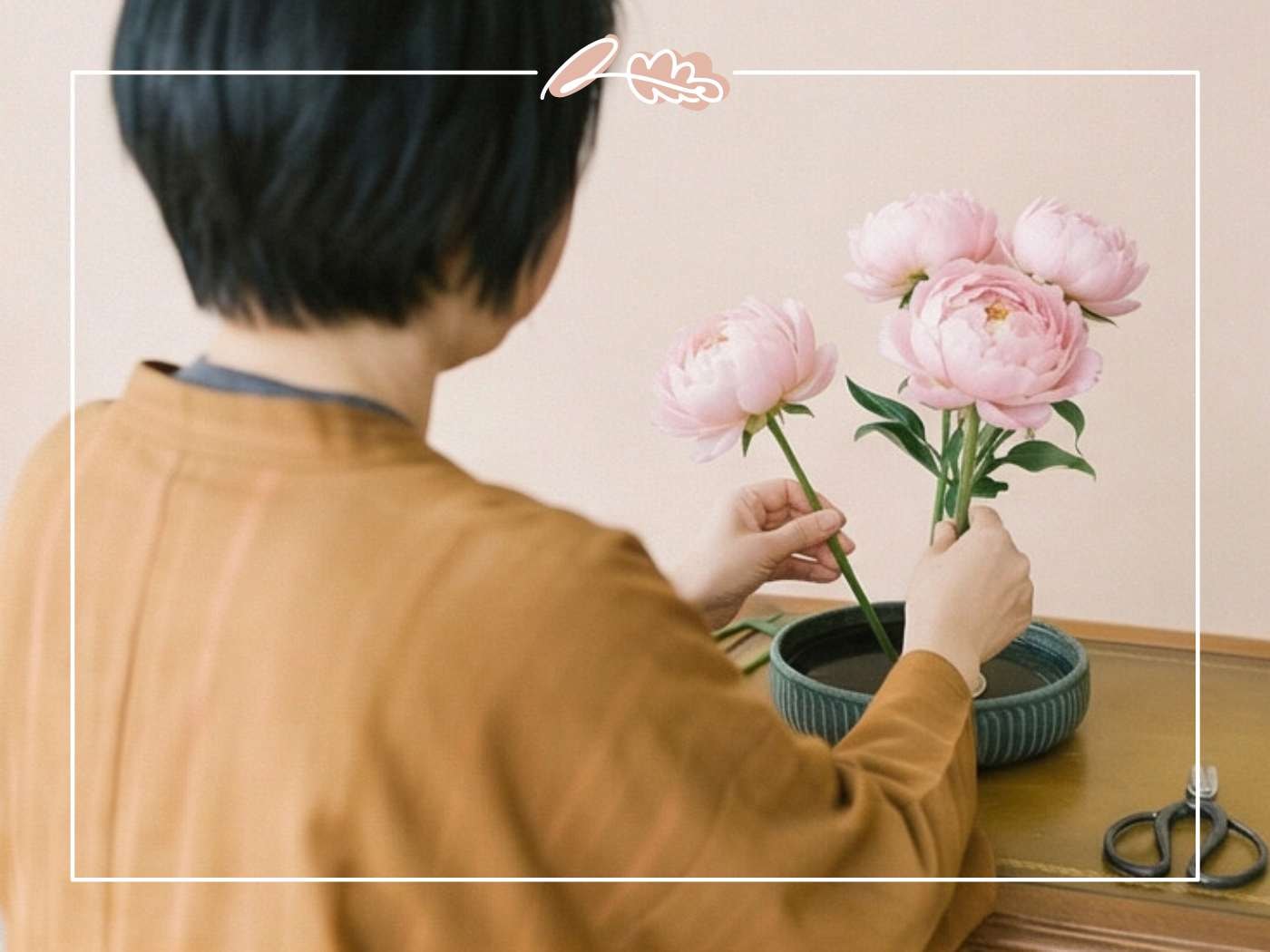 Woman viewed from behind arranging pink peonies in a ribbed teal ikebana vessel on a wooden table | Japanese Floral Art | Fabulous Flowers & Gifts