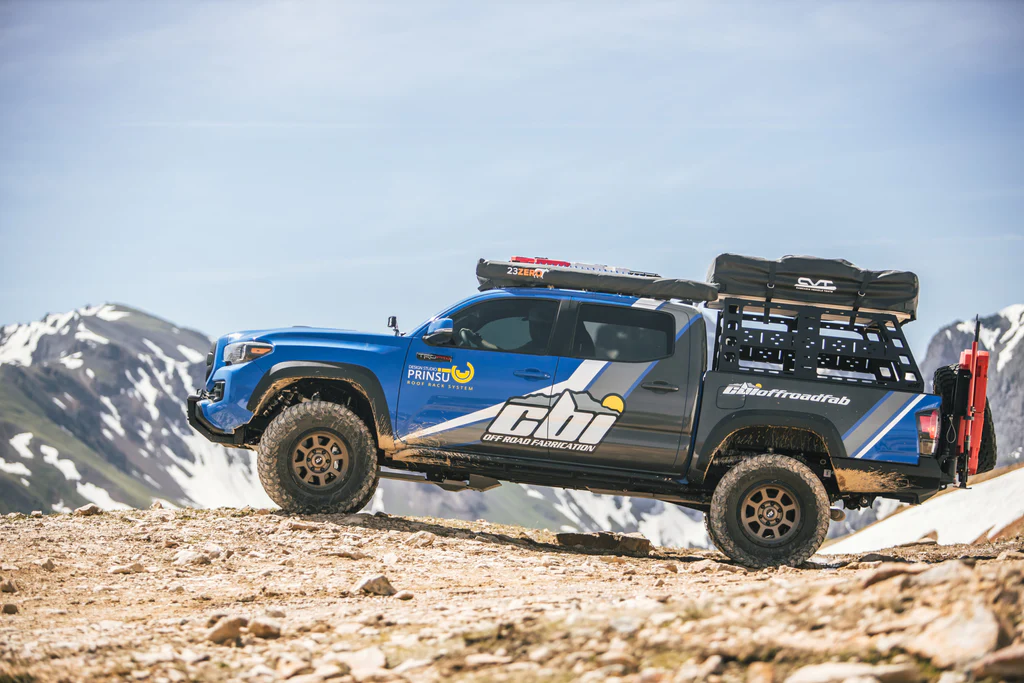 Off-Road Bed Rack on blue Toyota Tacoma with overlanding accessories.  Mountains in the background.