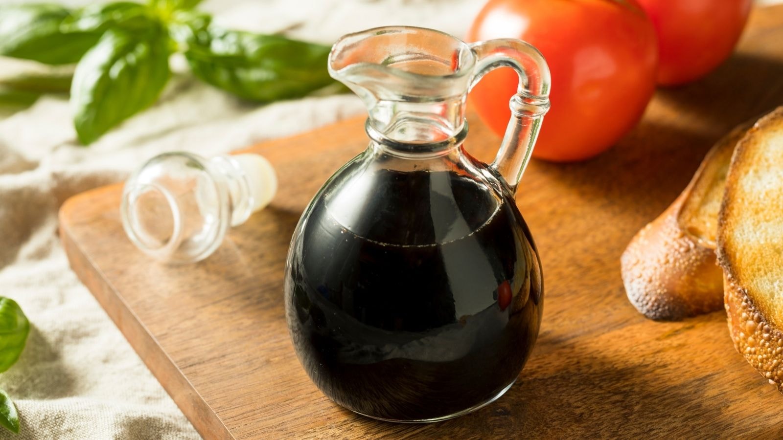 Bottle of balsamic vinegar next to fresh tomatoes and basil