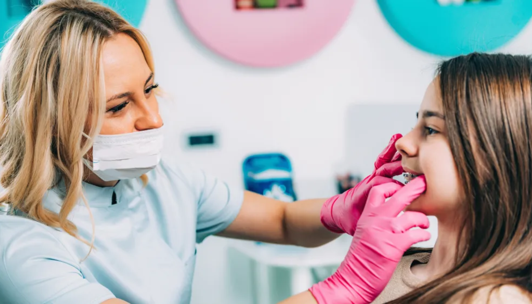 Tannlege med munnbind og rosa hansker undersøker jentas tenner.