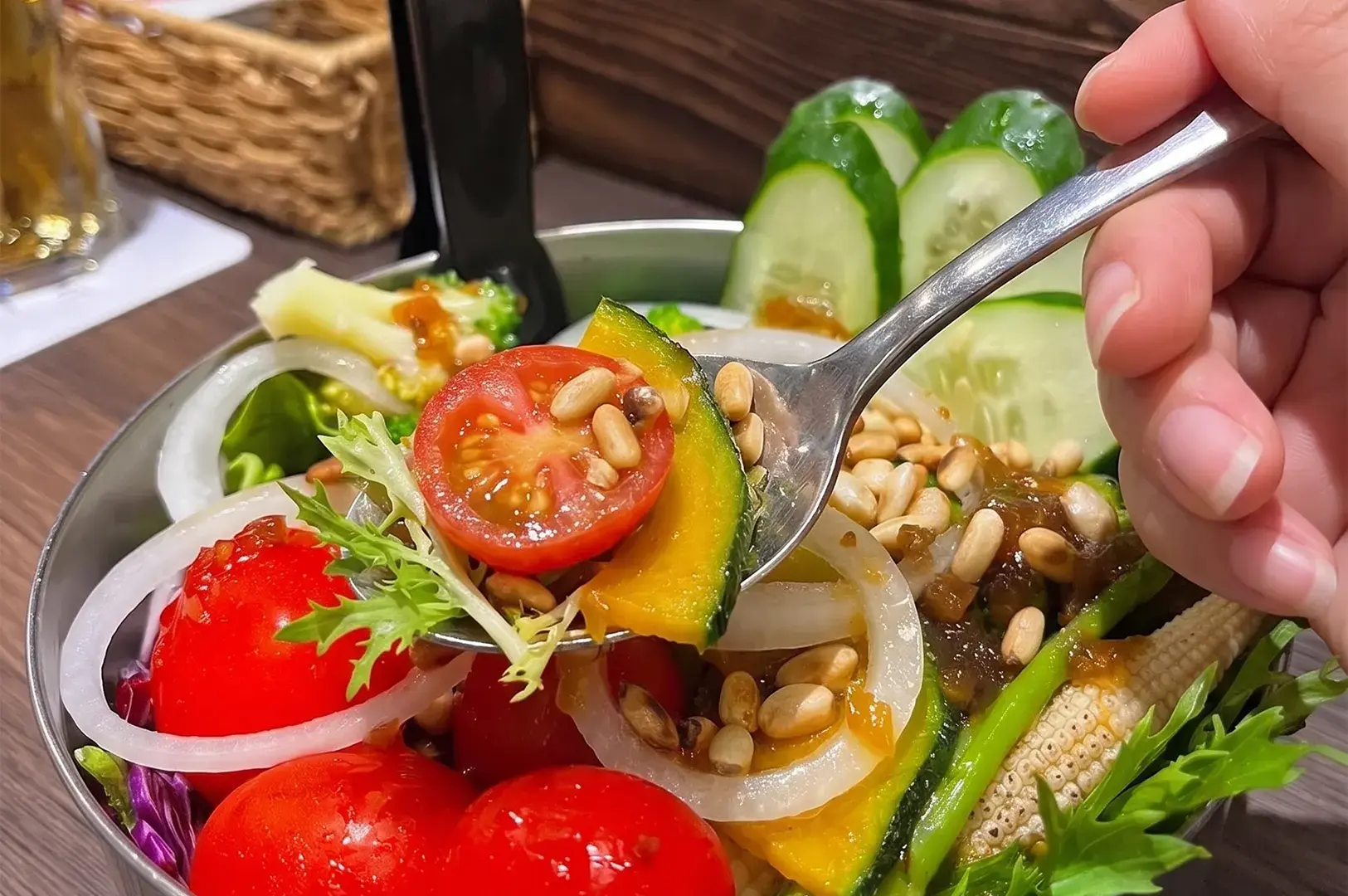 A close-up of a person holding a spoonful of fresh Japanese salad featuring tomatoes, pumpkin, cucumber, and pine nuts.