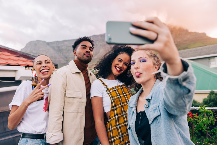 Group of young adults making faces for a selfie on a rooftop.