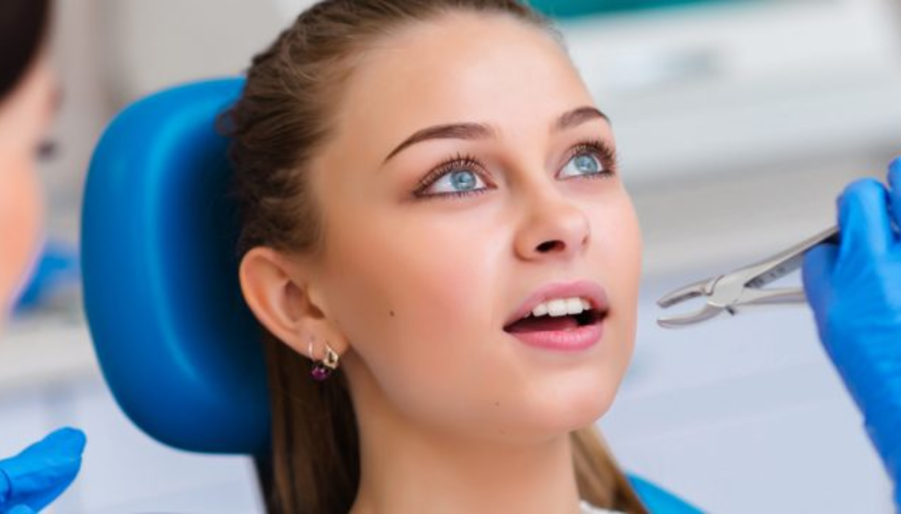 Ung pasient i tannlegestol blir undersøkt av tannlege med hansker.