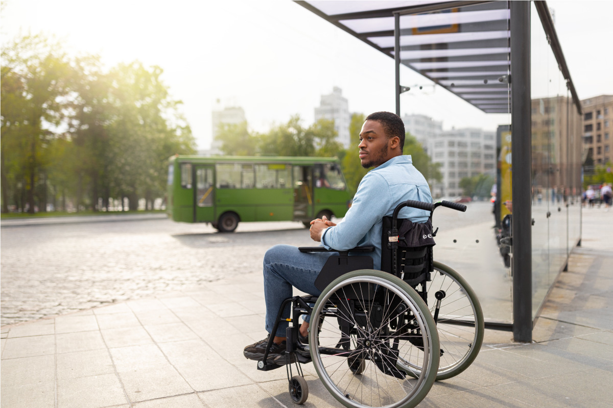 black man in wheelchair at bus stop waiting for paratransit bus