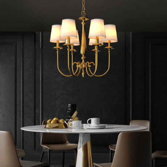A Hampton chandelier design with elegant gold arms and fabric lampshades hanging above a modern dining table, blending classic charm with contemporary sophistication.