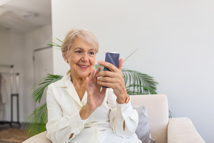 Cheerful elderly blond woman sending a text. 