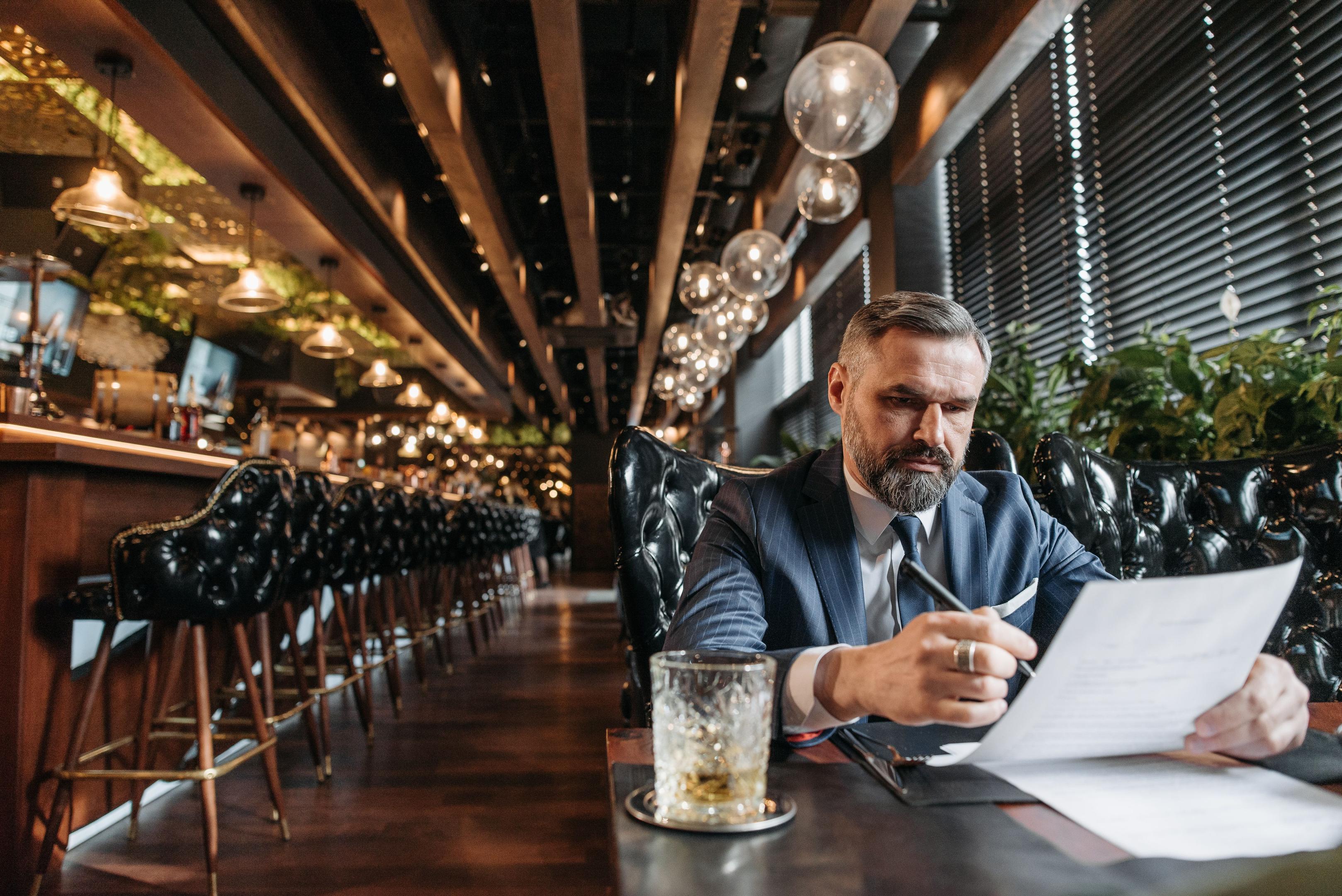 A restaurant owner is reviewing data on a tablet at the counter, with the bustling kitchen activity in the background, highlighting the importance of online reviews and customer feedback.