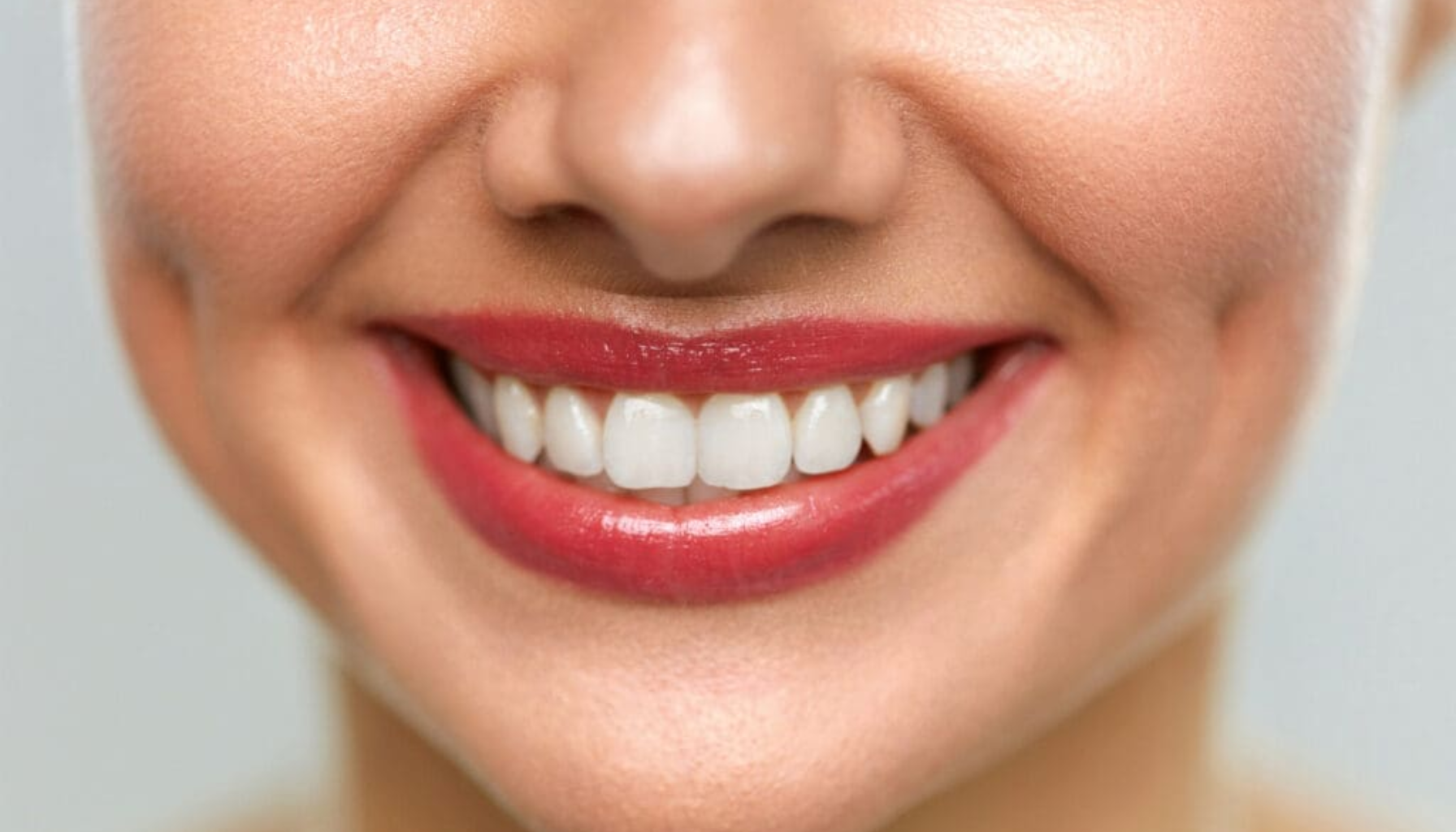 Fordeler Og Ulemper med Skallfasetter Uten Sliping 13 Nærbilde av smilende kvinne med røde lepper som viser hvite, rette og sunne tenner.