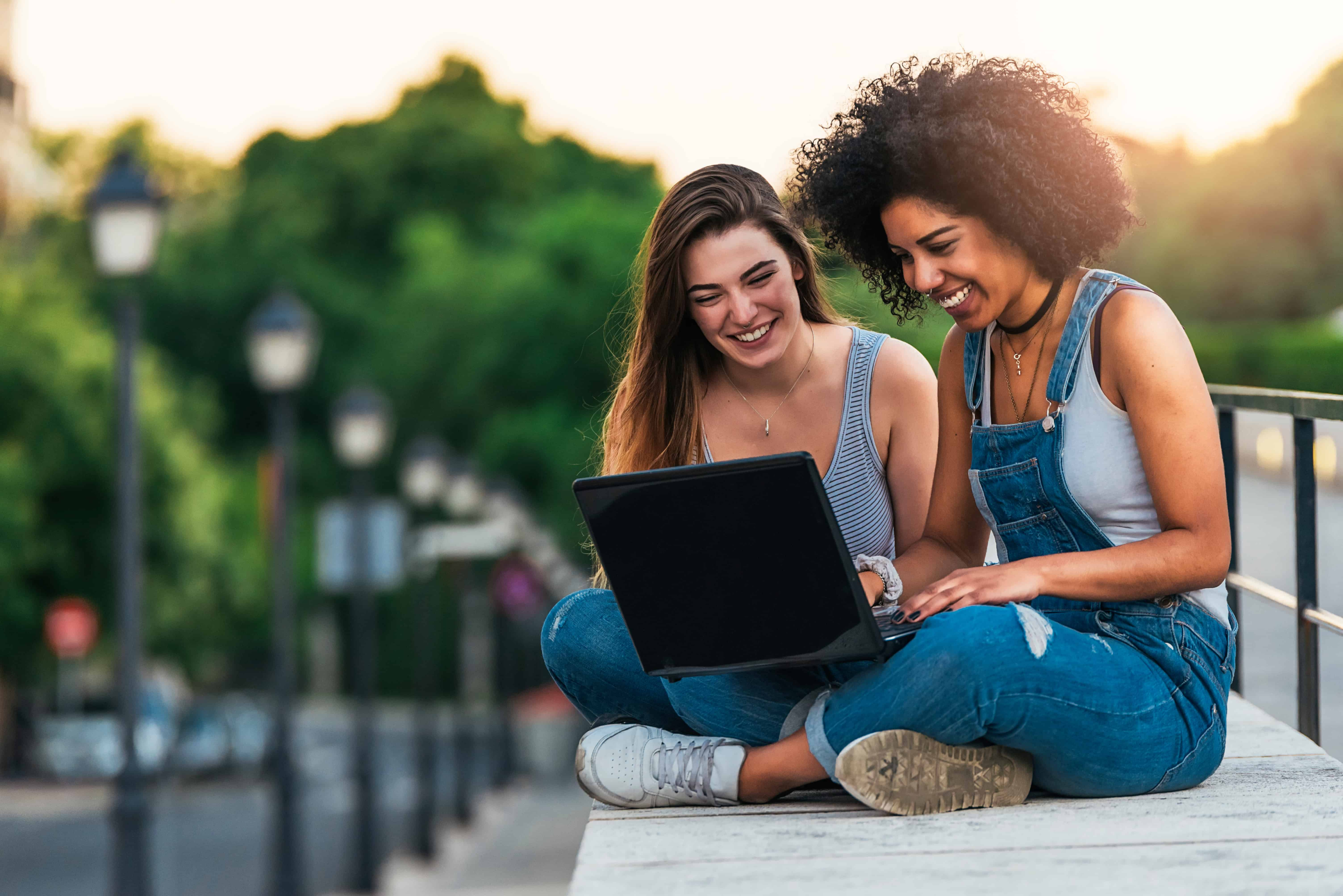 Two friends talking and hanging out. They are both looking at a laptop while they sit in New York City.