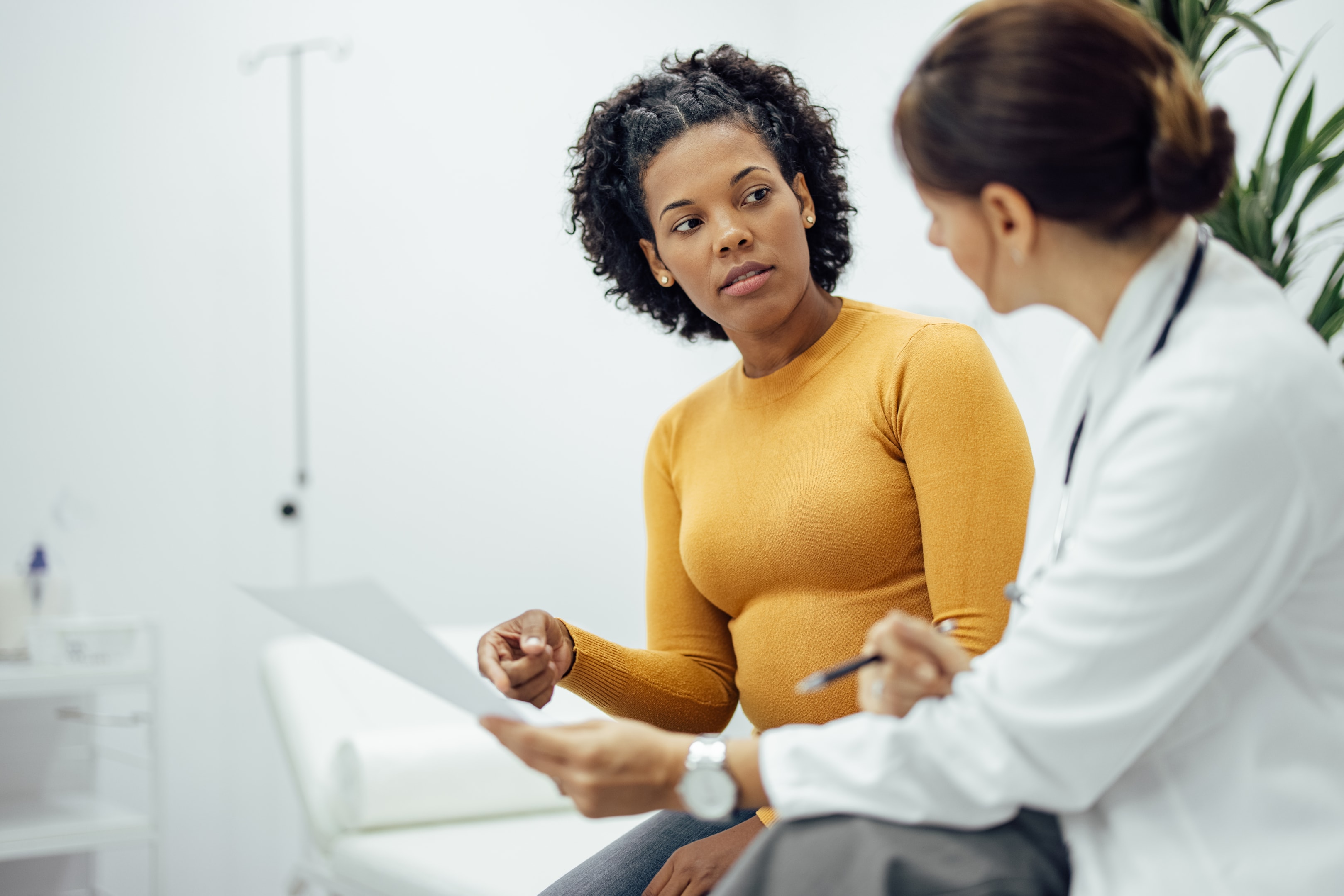 A woman in a clinical setting speaking with her gynecologist, both seated and engaged in conversation, representing informed decision-making and proactive care