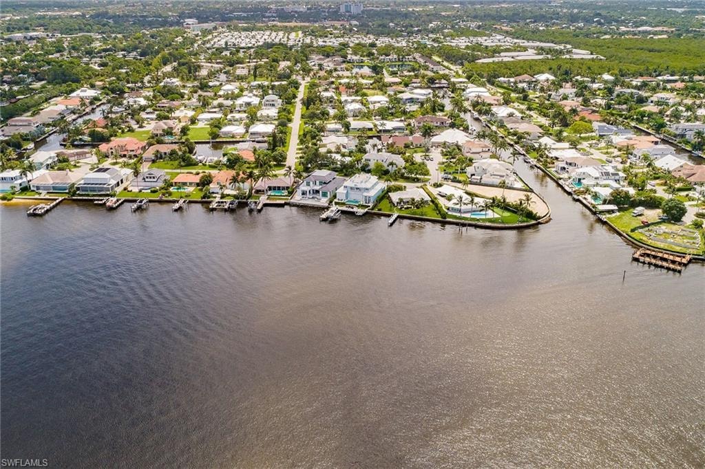 The image captures a stunning view of Naples Bay, showcasing the vibrant downtown Naples skyline in the background, with luxurious waterfront homes lining the shore. This picturesque scene highlights the coastal luxury and refined waterfront living that the prestigious Royal Harbor community offers.